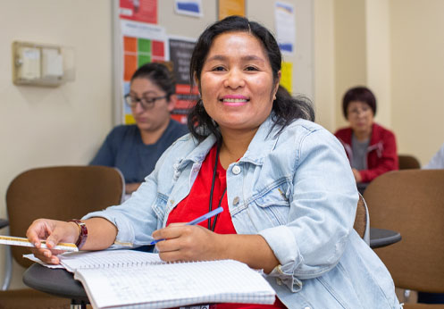A student smiling in her class, while taking notes.